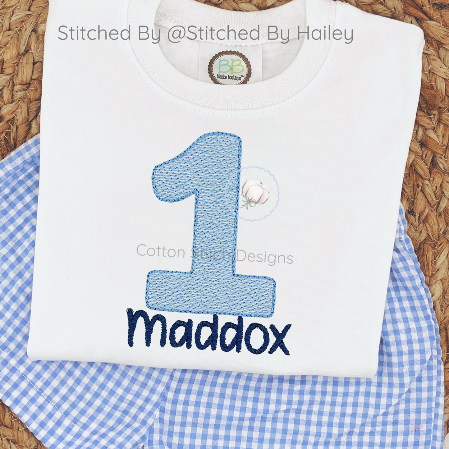 Machine Embroidery design Cotton Stitch Designs White shirt with blue number '1' and name 'Maddox' on a blue checkered fabric background.
