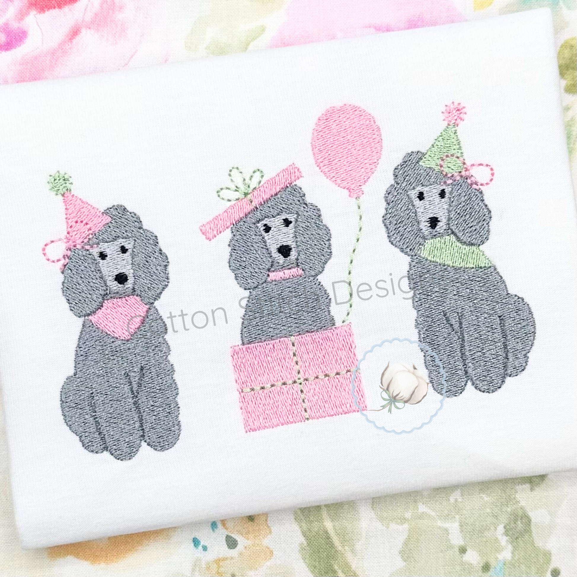 Machine Embroidery design Cotton Stitch Designs Embroidered design of three poodles with party hats and balloons on a white fabric background.